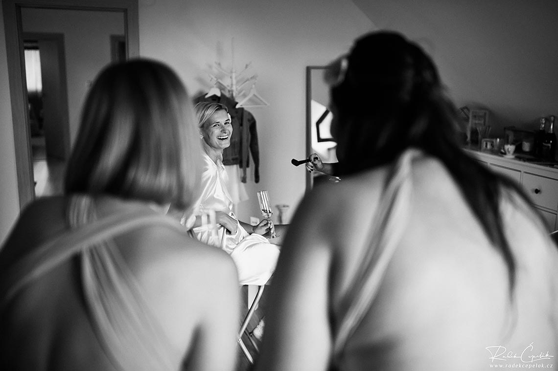 černobílá svatební fotografie nevěsty, jak se směje na družičky, momentka během příprav