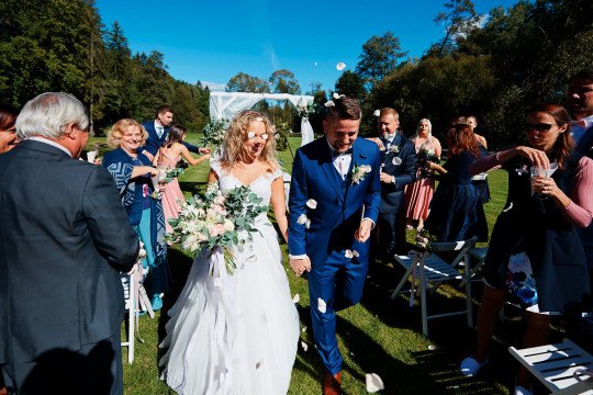 svatební fotografie novomanželů po obřadu v Hodějovickém mlýně, kteří procházejí uličkou mezi hosty
