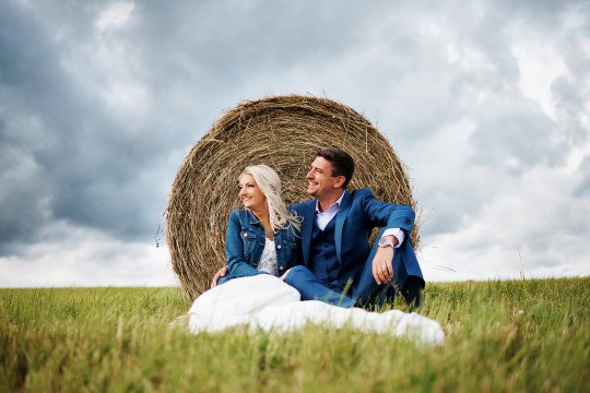 ženich a nevěsta sedí na poli s balíkem sena