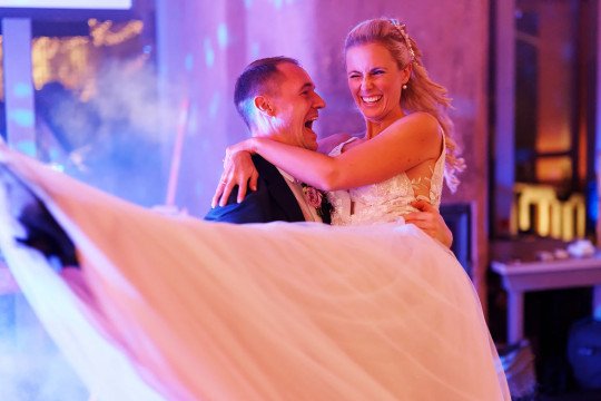 svatební fotografie nevěsty s ženichem během party, kde ženich drží nevěstu v náručí